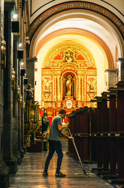 Inside the Ibarra Cathedral, a person cleans the polished floor, highlighting the vibrant altar and intricate decor.