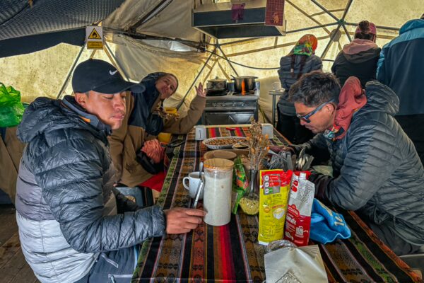 Travelers enjoy warm drinks and local cuisine inside a cozy tent at high camp near Chimborazo Volcano, Ecuador.