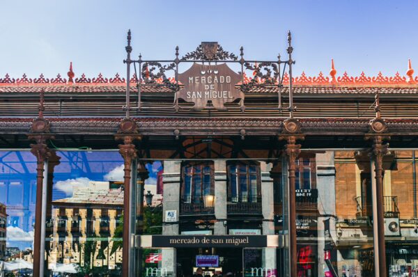 Mercado de San Miguel features intricate ironwork and vibrant reflections, showcasing a lively atmosphere in Madrid, Spain.