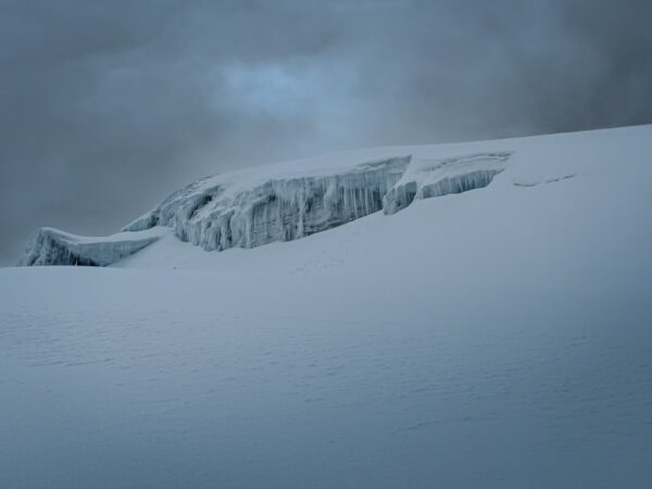 Snow-covered peak with glistening ice against a cloudy sky at Mount Cotopaxi, Ecuador, showcasing its rugged beauty.