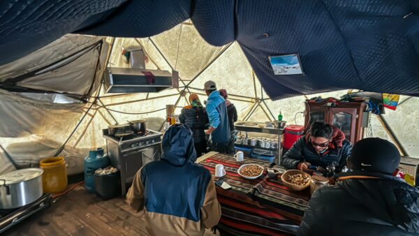 High camp at Chimborazo Volcano, Ecuador, featuring climbers enjoying a meal in a geodesic dome, with cooking equipment visible.