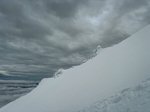 Snow-covered slopes and dramatic, cloudy skies at Mount Cotopaxi, Ecuador, creating a serene, majestic winter landscape.
