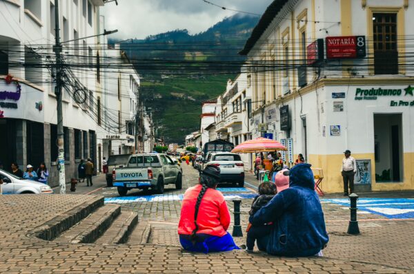 Colorful scene at Parque Pedro Moncayo in Ibarra, Ecuador, with locals gathered on the cobblestone street, shops lining the road.