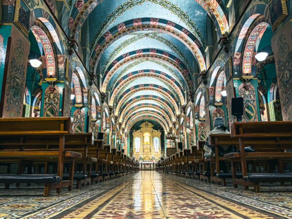 Vibrant interior of Iglesia Santiago Apostol in Machachi, Ecuador, featuring ornate arches and colorful murals with wooden benches.