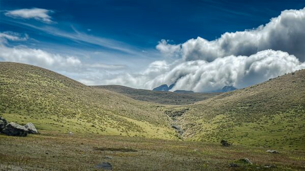 Lush green hills meet a vibrant blue sky with dramatic clouds in Cotopaxi National Park, Ecuador.
