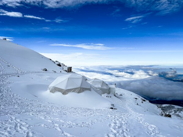High camp tents nestled in snow against a backdrop of Chimborazo Volcano, with expansive skies over Ecuador.