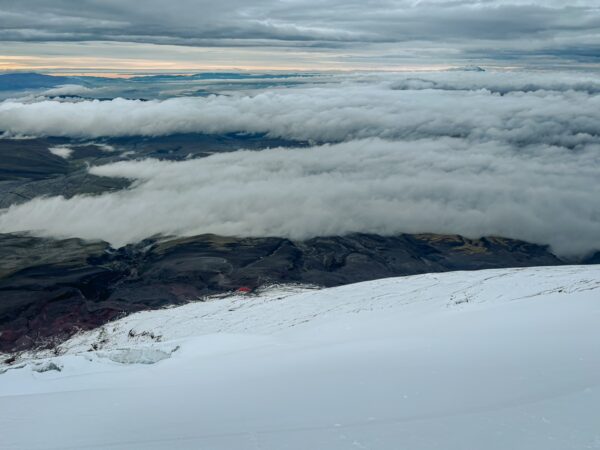 Snow-covered slopes descend into a sea of clouds below Mount Cotopaxi, creating a stunning vista of contrasting textures and colors.