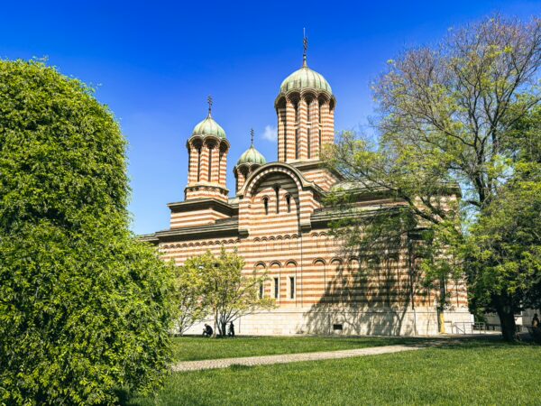 Saint Demetrius Cathedral showcases its distinctive striped brickwork and domes amidst lush green trees in Craiova, Romania.