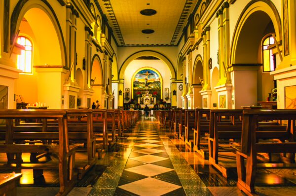 Sunlight streams through stained glass windows in San Francisco de Asís Church, highlighting elegant arches and polished wood pews in Tulcán, Ecuador.