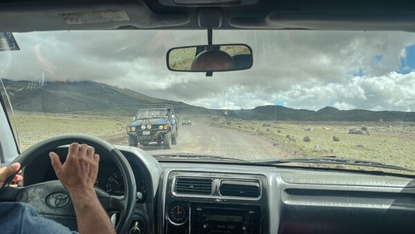 Off-road vehicles navigate a rugged track in Cotopaxi National Park, Ecuador, with picturesque mountains under a cloudy sky.