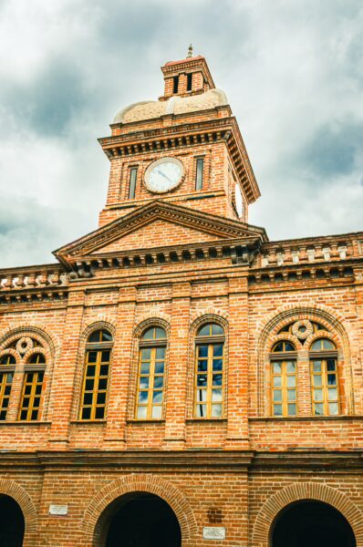 Historic brick building with clock tower and arched windows, set against a cloudy sky in Ibarra, Ecuador.