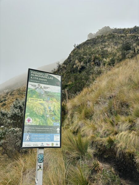 Trail sign near Imbabura Volcano, Ecuador, surrounded by lush greenery and misty mountains in the background.