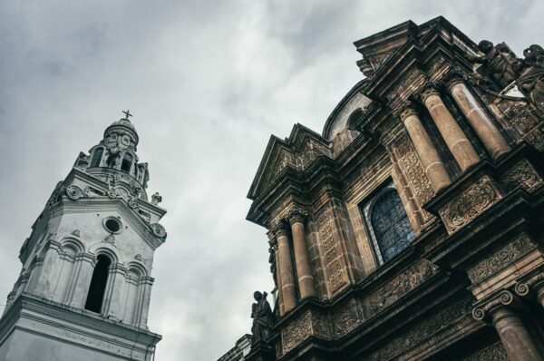 Majestic colonial architecture with ornate details and a bell tower under a dramatic cloudy sky in Quito, Ecuador.