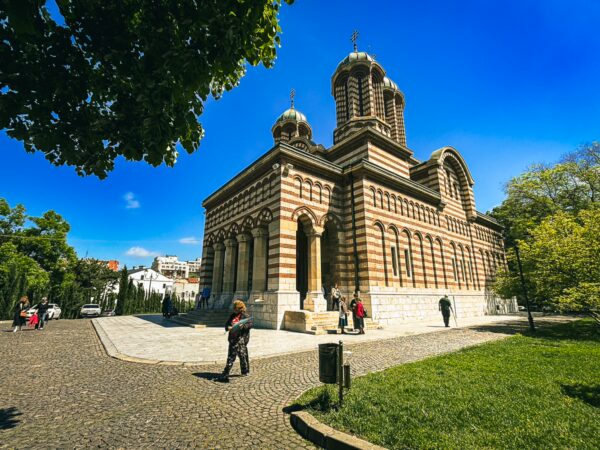 Saint Demetrius Cathedral in Craiova features distinctive striped stone architecture against a bright blue sky and green surroundings.