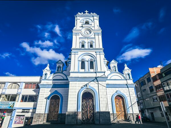 White and blue cathedral stands tall against a bright sky in Tulcan, Ecuador, showcasing intricate architectural details.