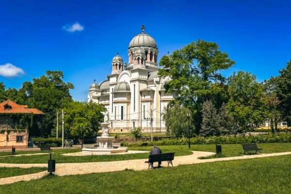 Majestic Church of Our Lady stands amidst lush greenery in Craiova, Romania, with a clear blue sky enhancing the serene park atmosphere.