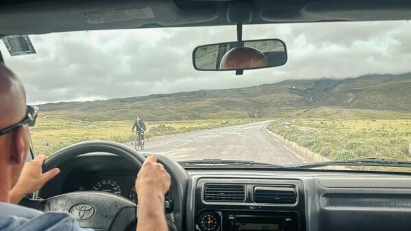 Driving through Cotopaxi National Park, Ecuador, with lush greenery and an expansive road ahead under a cloudy sky.