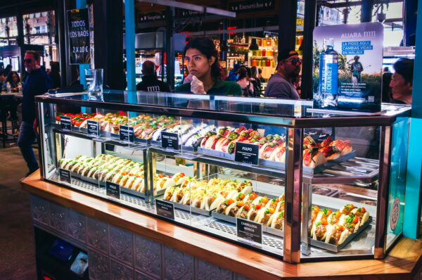 Colorful tapas display at Mercado de San Miguel in Madrid, featuring a variety of vibrant dishes and a visitor enjoying the scene.