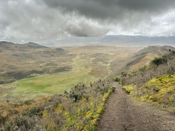 Lush green valleys and rugged terrain under a dramatic sky at Volcán Rumiñahui, Ecuador, with a winding dirt path.