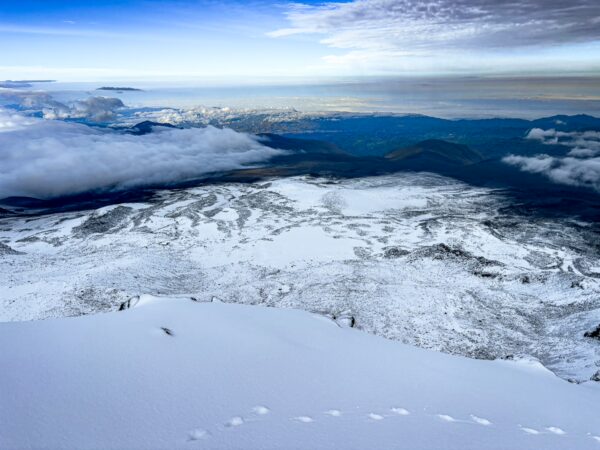 Snow-covered slopes of Chimborazo volcano in Ecuador, with a panoramic view of distant mountains and a sky blending blue and white.