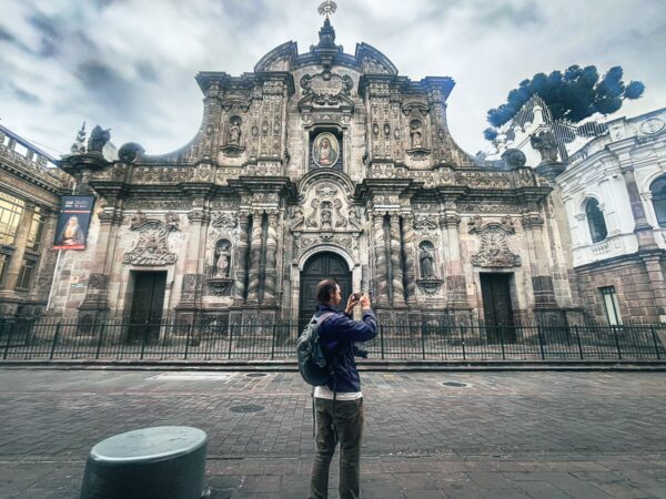 Capturing the intricate facade of the Church of the Society of Jesus, as a visitor admires its ornate details in Quito, Ecuador.