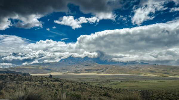 Cotopaxi National Park showcases expansive grasslands under a dramatic sky, with the imposing Cotopaxi volcano in the distance.