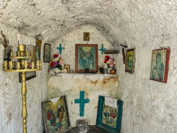 Charming shrine in Lagadia, Arcadia, Greece, featuring colorful icons, candles, and stone walls with blue crosses.