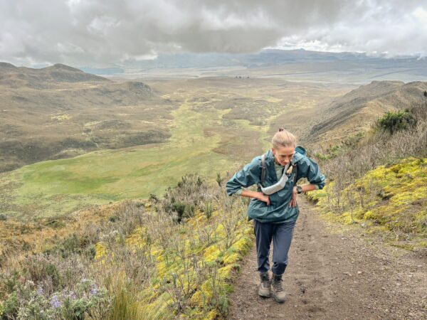 Hiker navigating a trail with lush greenery and dramatic rolling hills in the Rumiñahui region, Ecuador.