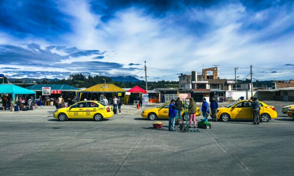 Vibrant yellow taxis line the bus station in Tulcán, Ecuador, with colorful market stalls and a scenic sky in the background.