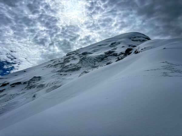 Snow-covered slopes and looming clouds create a dramatic scene at Chimborazo Volcano, Ecuador, highlighting its majestic peak.