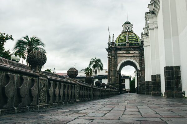 Elegant green dome atop the entrance archway, flanked by palm trees and ornate stonework at the Metropolitan Cathedral, Quito.