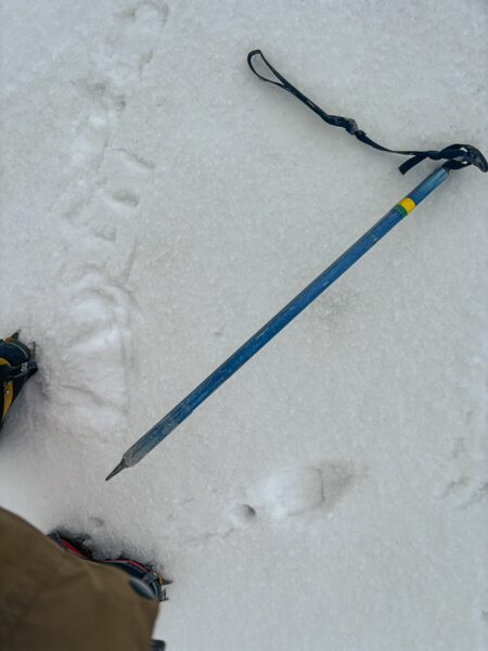 Crampon-clad boots leave footprints in the snow beside a blue ice axe on the snowy slopes of Mount Cotopaxi, Ecuador.
