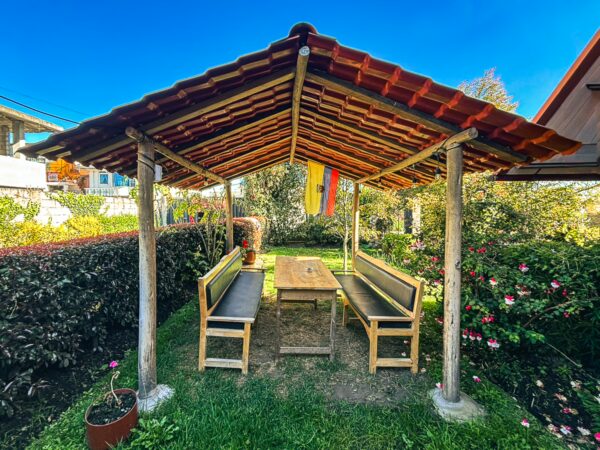 Casa del Montanero features a rustic, shaded seating area with wooden benches and a table, surrounded by lush greenery in Machachi, Ecuador.