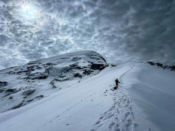 Snow-covered slopes lead up to Chimborazo Volcano, with dramatic clouds overhead creating a moody atmosphere.