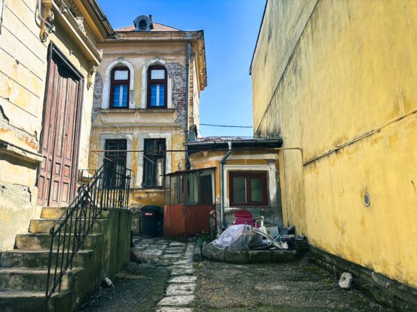 Old buildings with yellow walls and weathered facades line a narrow alleyway in Craiova, Romania, featuring a staircase and scattered debris.