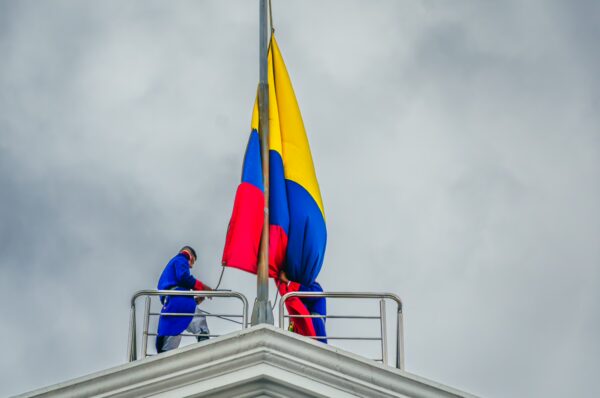 Workers adjust the Colombian and Ecuadorian flags atop Carondelet Palace in Quito, Ecuador, under a cloudy sky.