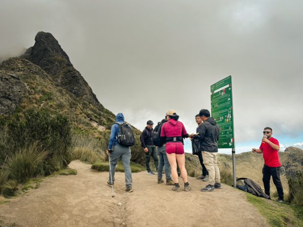 Hikers gather at a trailhead near Pichincha Volcano, surrounded by rugged terrain and cloudy skies in Ecuador.
