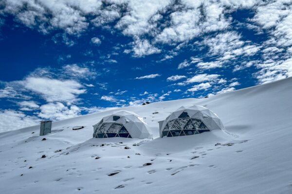 White geodesic domes stand out against a snow-covered landscape under a blue sky at Chimborazo Volcano, Ecuador.