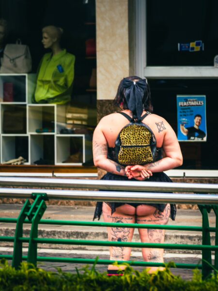 A person in a leopard print outfit sits against a railing, with a shop display featuring mannequins in the background in Ibarra, Ecuador.