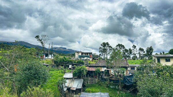 Lush green fields surround rustic homes under a cloudy sky in Machachi, Ecuador, highlighting local rural life.