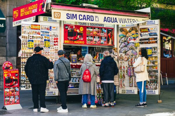 Colorful souvenir stand with bustling tourists in Madrid, Spain, showcasing various trinkets and SIM card options.