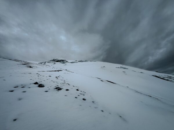 Snow-covered slopes and dramatic, cloudy skies at Mount Cotopaxi, Ecuador, create a striking, serene landscape.