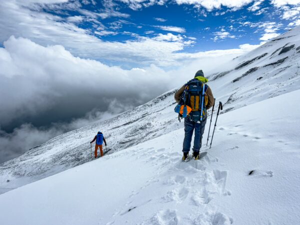 Snow-covered slopes of Chimborazo Volcano in Ecuador, with climbers navigating the terrain under a dramatic sky.