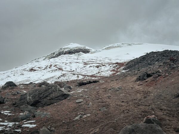 Snow-covered peaks and rocky terrain under a cloudy sky at Mount Cotopaxi, Ecuador, showcasing the rugged landscape.