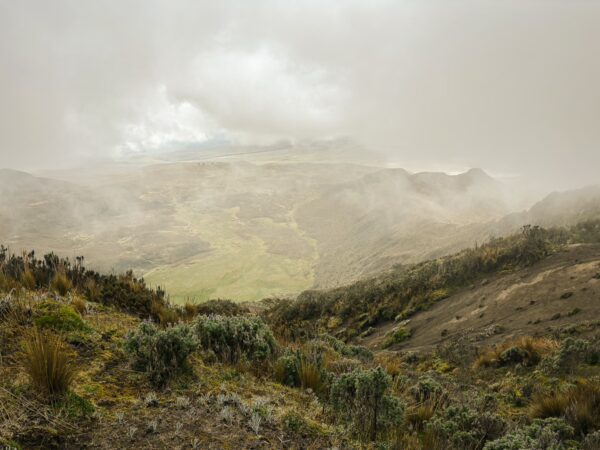 Volcan Ruminahui's misty landscape reveals lush green valleys and rugged terrain under a cloudy sky in Ecuador.