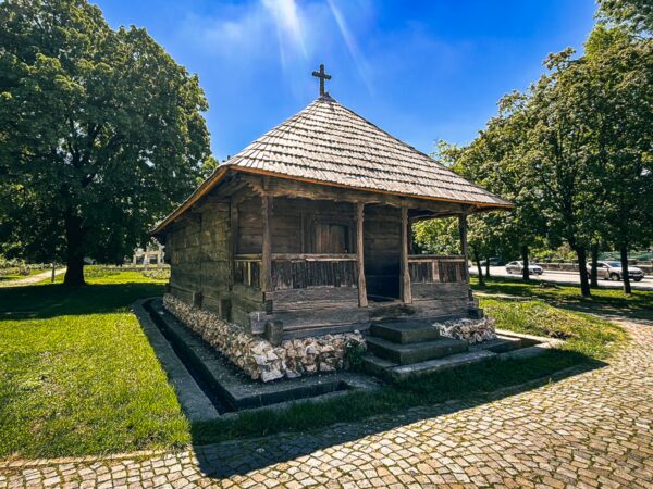 Wooden structure with a thatched roof set in lush greenery, showcasing rustic architecture in Craiova, Romania.