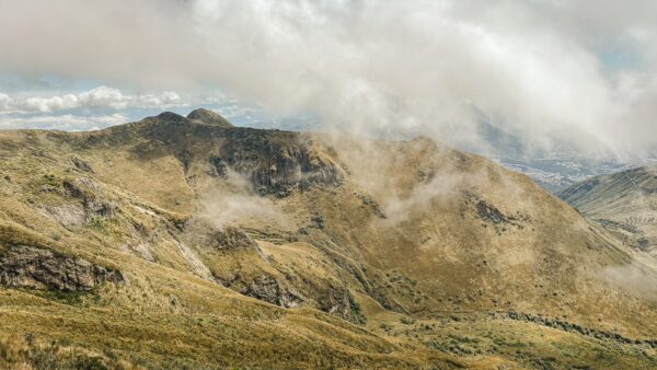 Majestic Pichincha Volcano in Ecuador, with rolling green hills and misty clouds enveloping the rugged landscape.