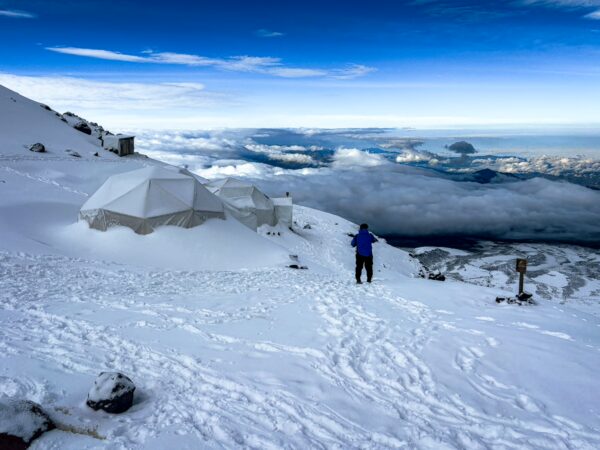 High camp tents surrounded by snow at Chimborazo Volcano, with a breathtaking view of clouds and the distant landscape of Ecuador.