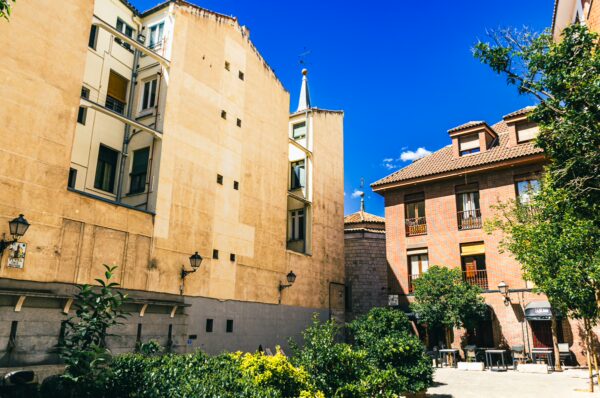 Plaza del Biombo features sunlit buildings with colorful facades and greenery, creating a charming urban retreat in Madrid.