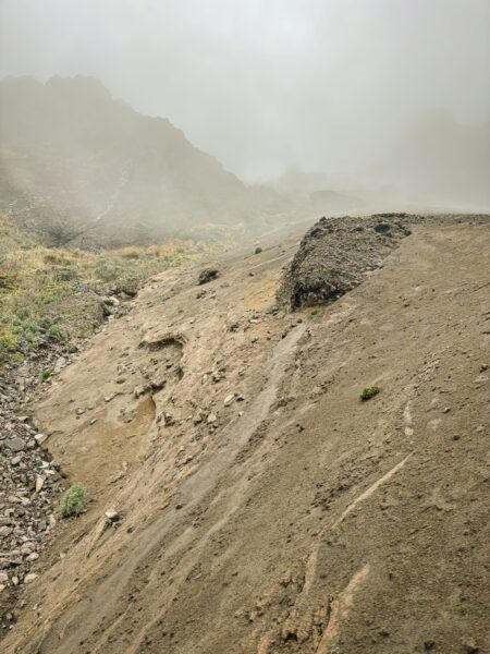 Volcanic terrain at Raminahui, Ecuador, features rocky slopes and misty, cloud-covered surroundings.